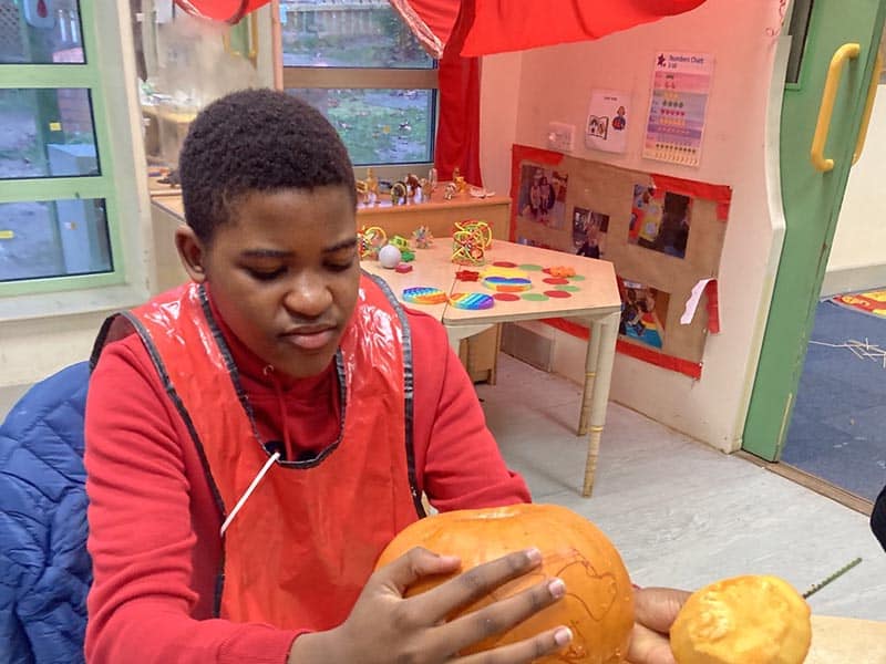 Young person in a classroom with a pumpkin