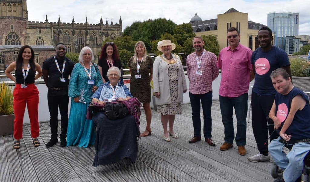 a photo of the WECIL team, Jayne can be seen sat in the front on a wheel chair, there are 10 people standing behind her, the photo is taken in Bristol city centre