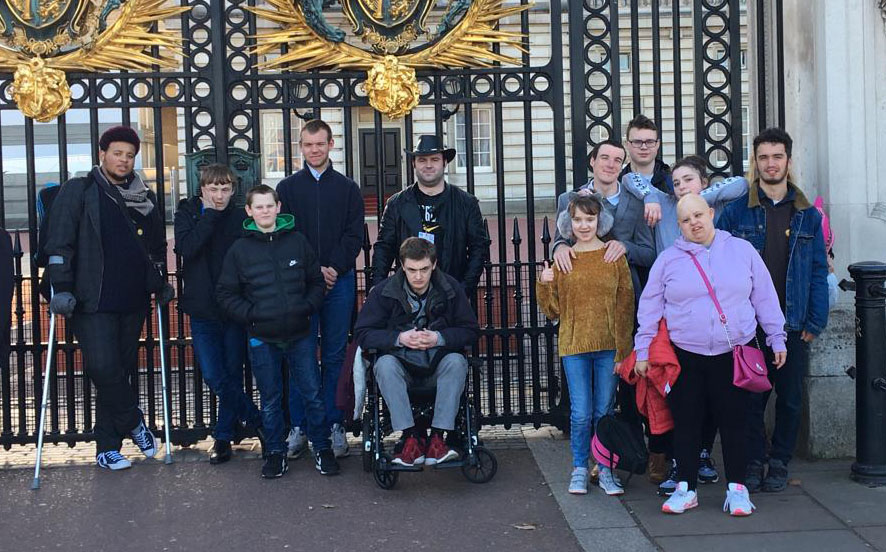 a group of young people, some with visible disabilities, are standing next to a big gate near parliament in London. Some look happy, some look serious!