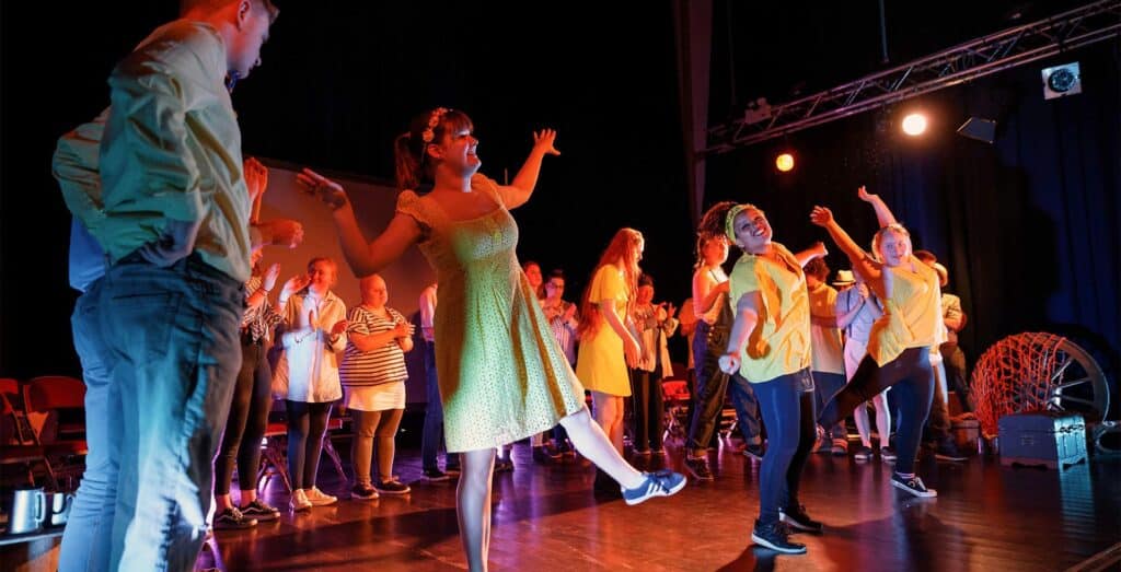 A stage performance of young Disabled People dancing and clapping
