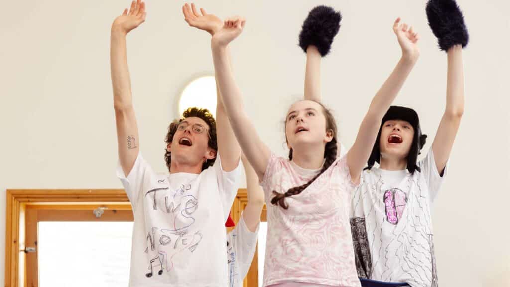 Three young people expressively putting their arms in the air at a drama youth group